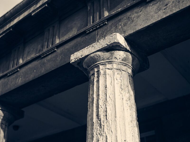 Close view of a weathered stone column meeting a shadowed entablature — neoclassical architectural detail in warm light.